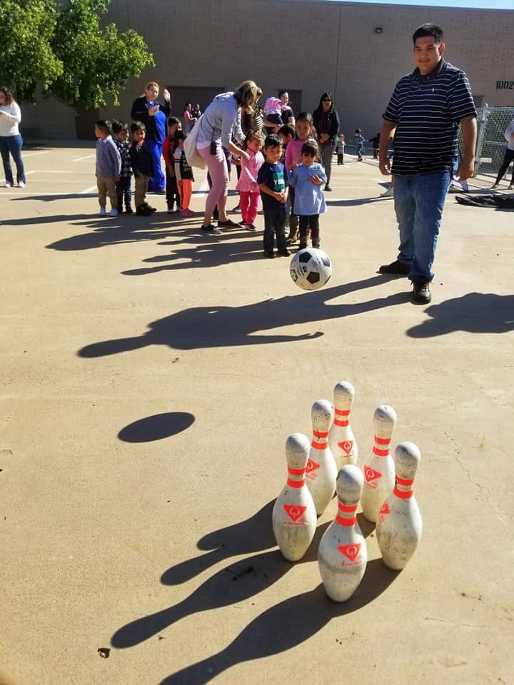 People and children playing outdoor bowling with a soccer ball