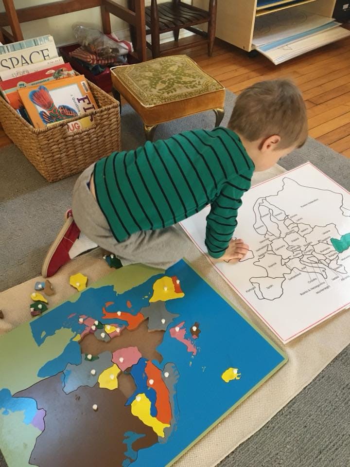 Child on floor looking at a map puzzle and a map outline