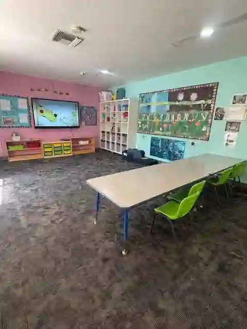 Classroom with a large screen, shelves, tables, and green chairs