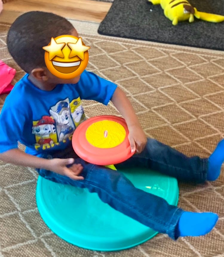 Child sitting on a teal balance board holding a frisbee
