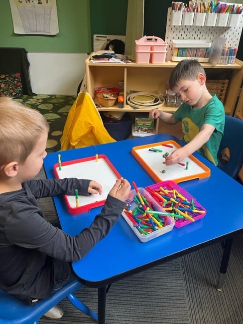 Two children playing with magnetic sticks and boards at a blue table