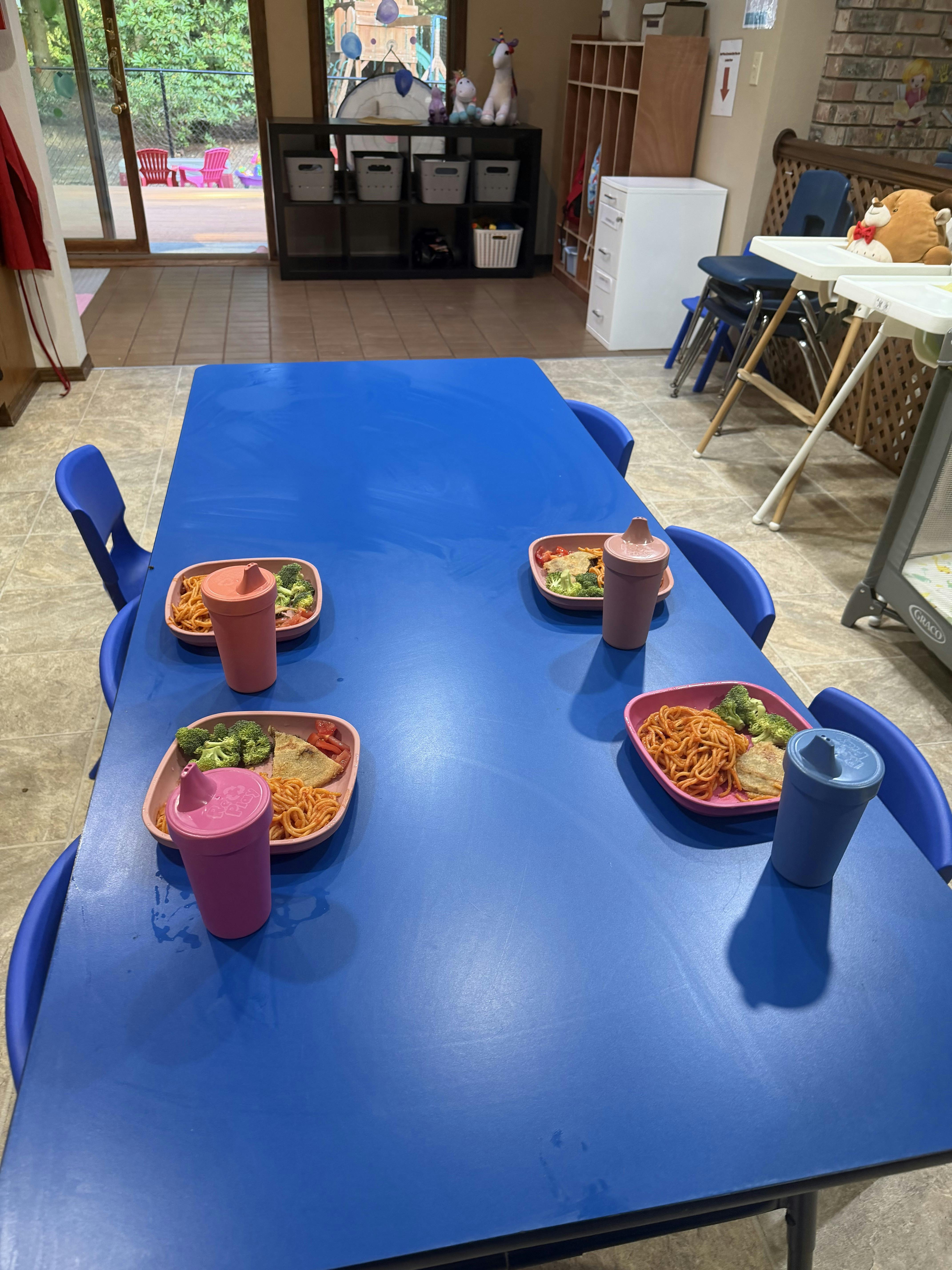 Four plates with spaghetti and broccoli set on a blue table in a playroom