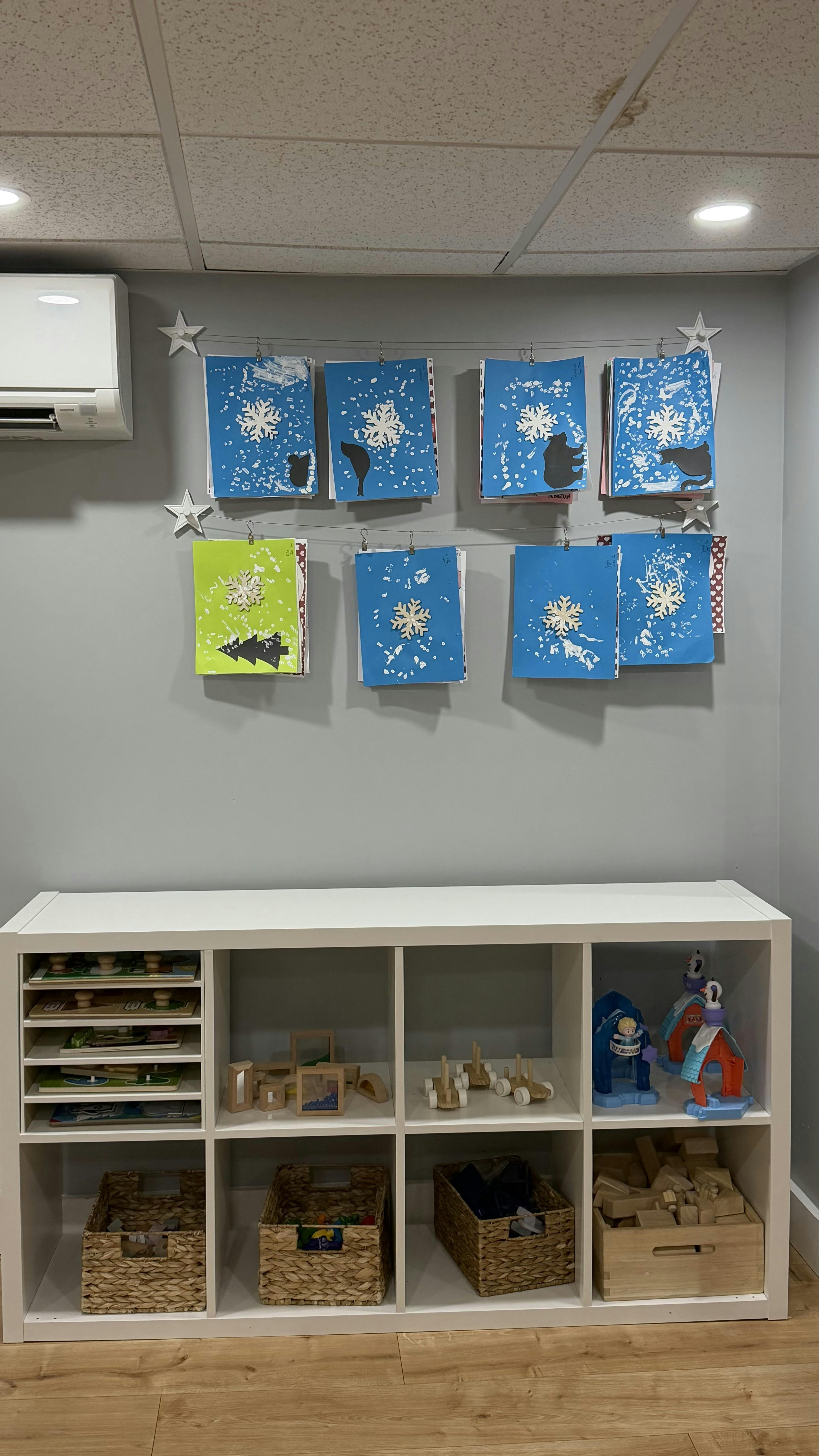 Children’s artwork featuring snowflakes and animal silhouettes displayed above toy storage