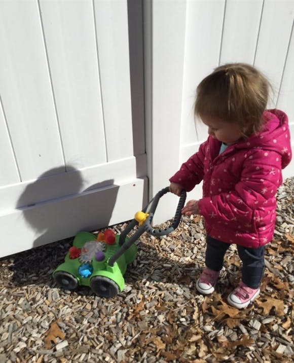 Child in a pink coat pushing a toy lawnmower
