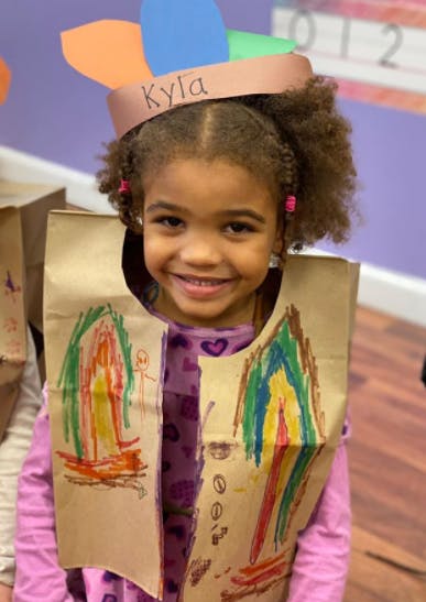 Child wearing a paper headdress with "Kyla" written on it and a decorated paper vest