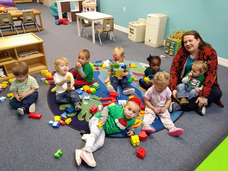 Adult and multiple children playing with blocks on a rug in a classroom