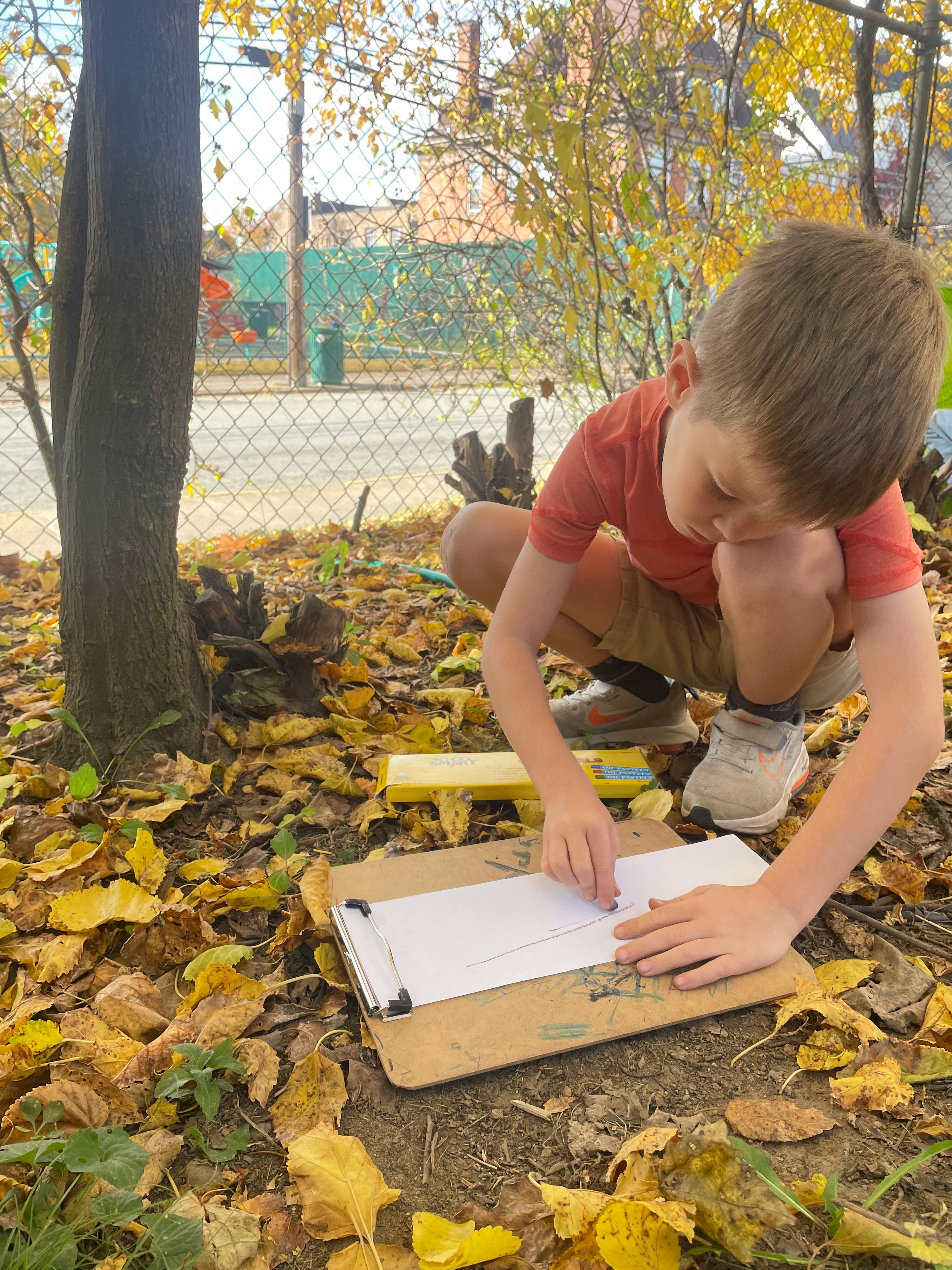 Child crouching, drawing on paper with crayons outdoors