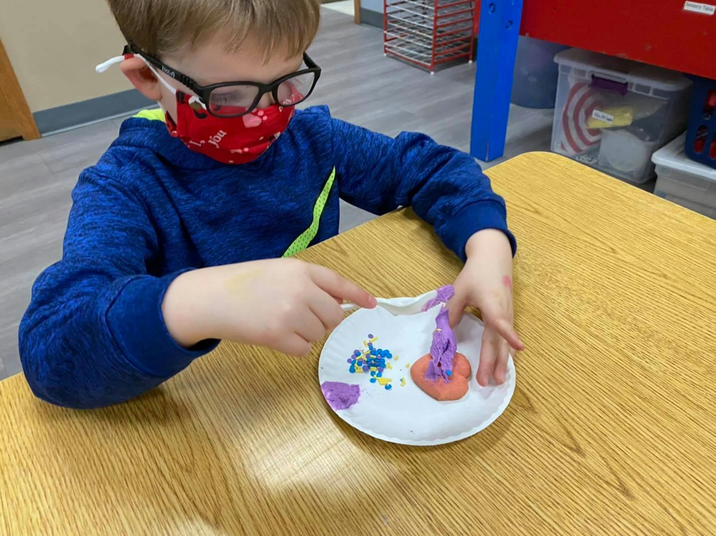 Child in a mask and glasses decorating a craft on a paper plate