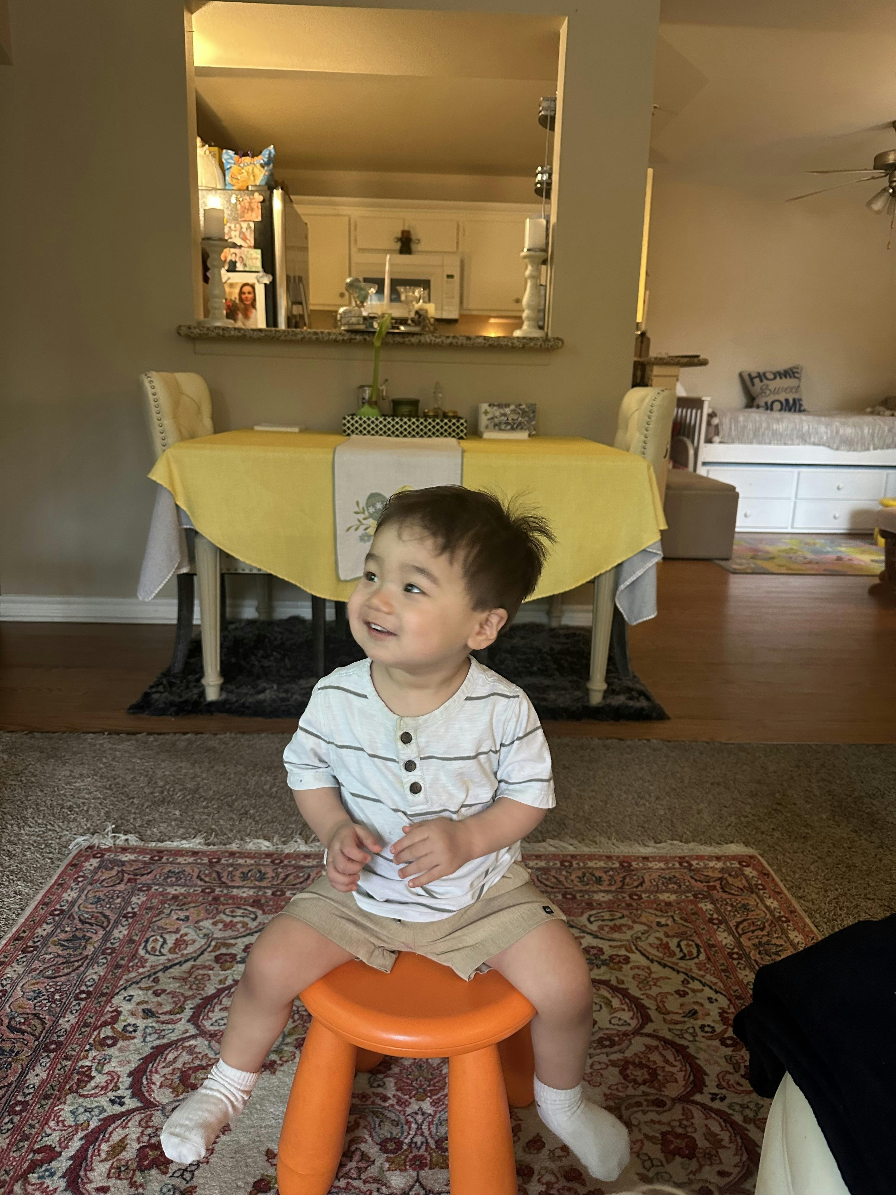 A young child sitting on a small orange stool
