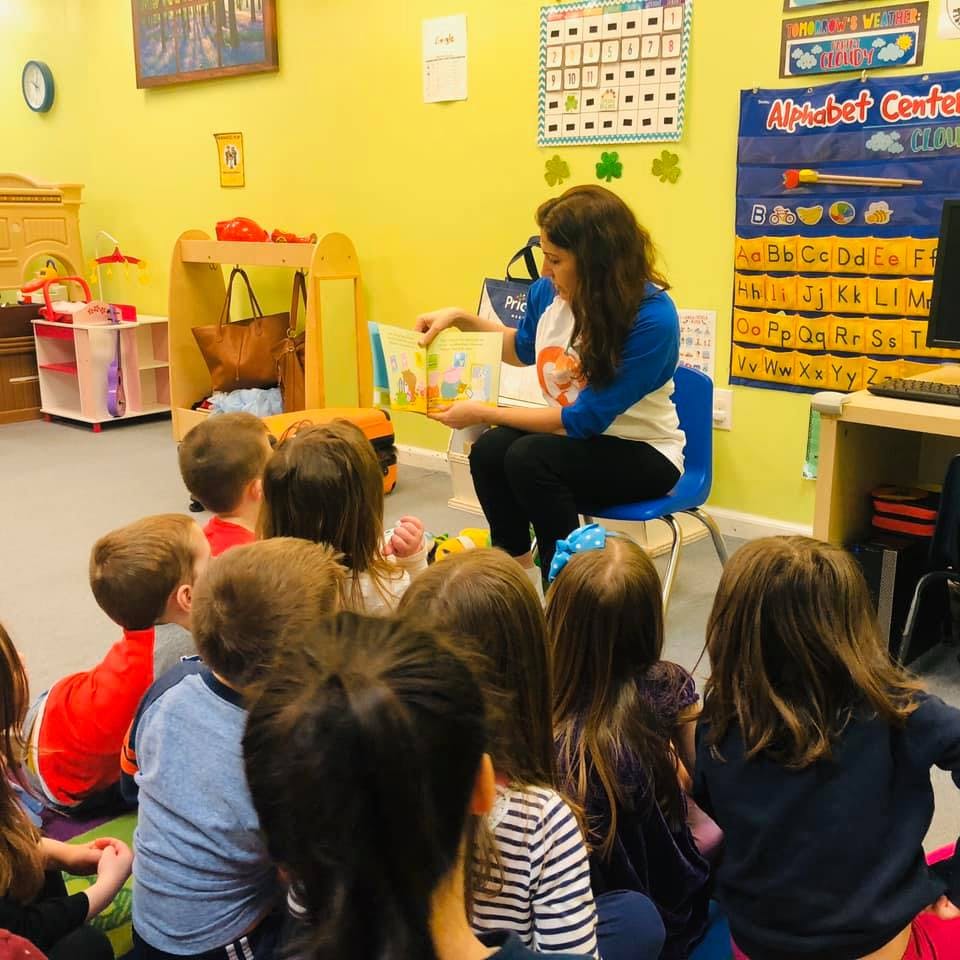 Person reading a book to a group of children in a classroom
