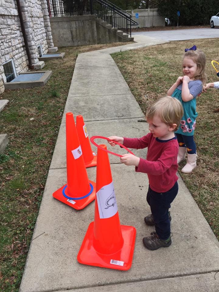 Child holding a red ring over an orange cone, cone-shaped object