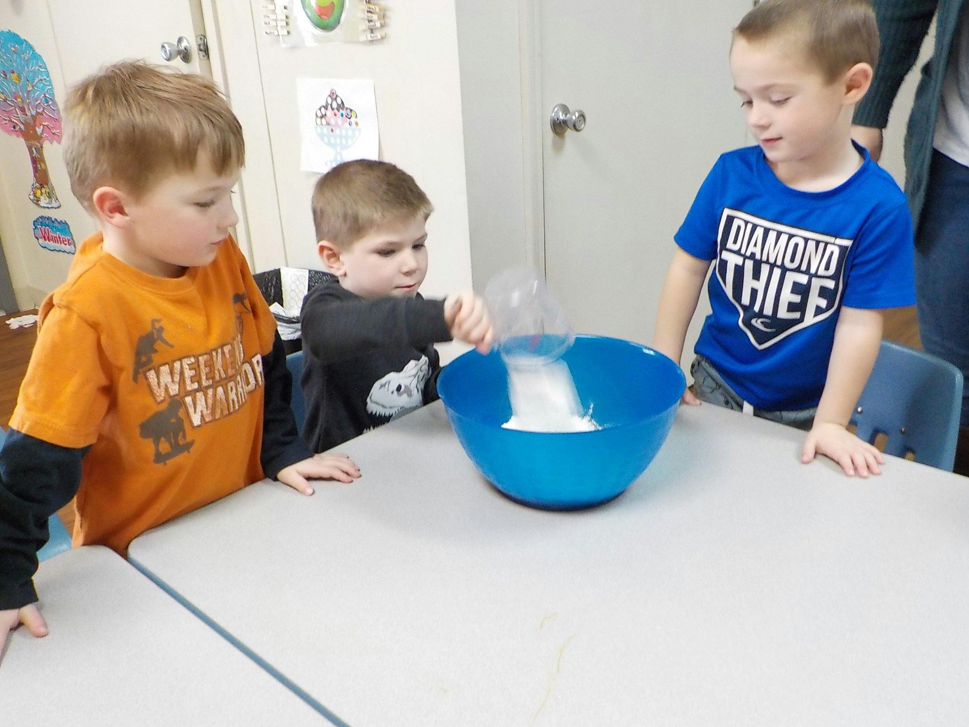 Three children gathered around a blue bowl on a table