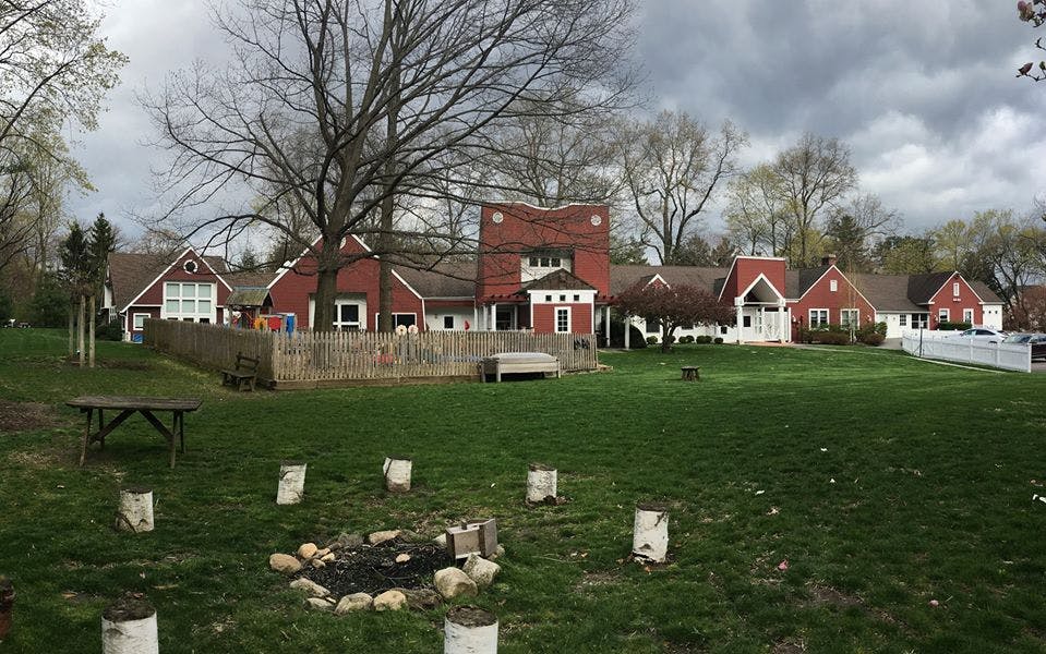 Grassy field with a fire pit and red buildings in the background