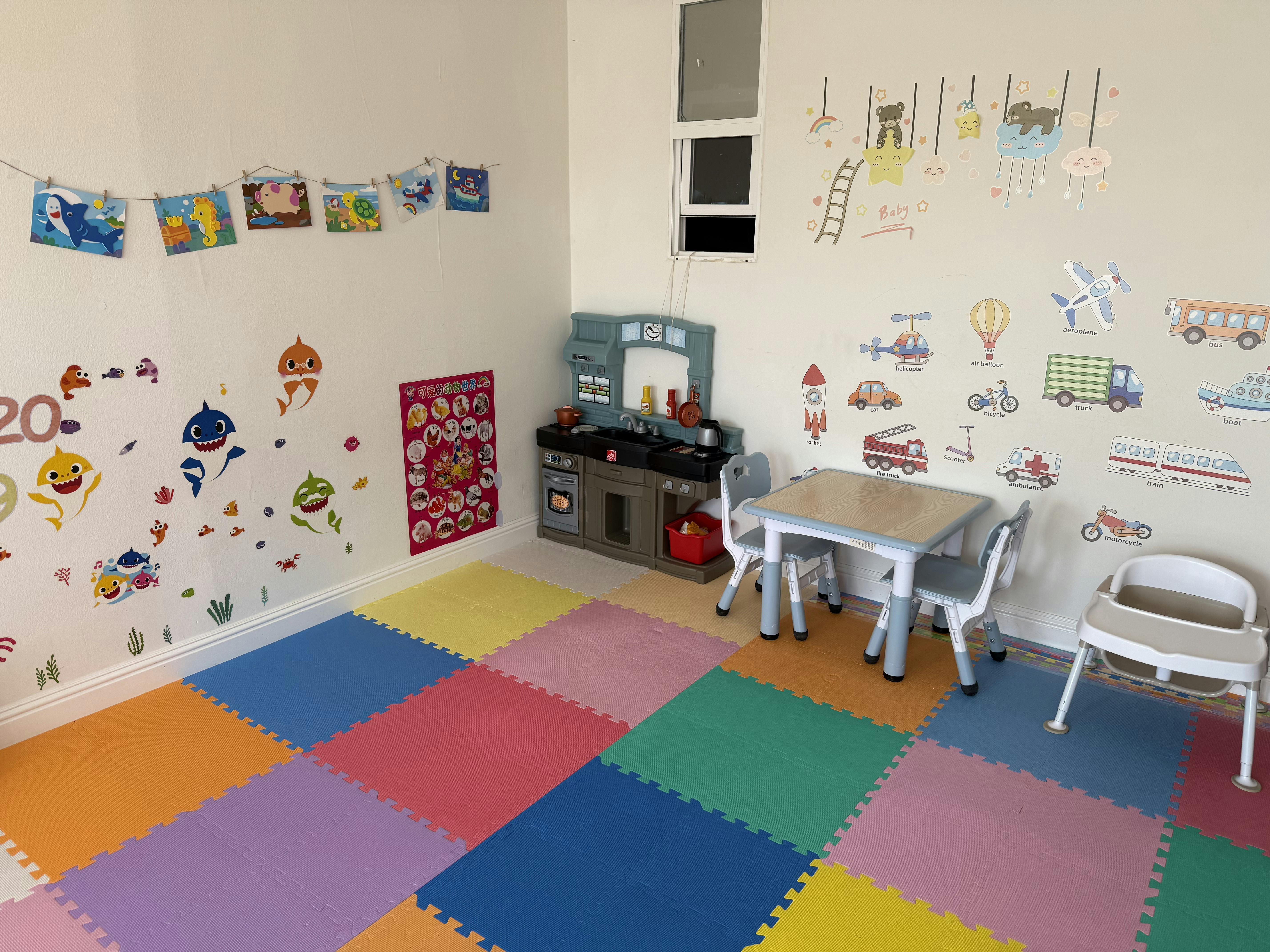 Playroom with colorful floor mats, toy kitchen, small table and chairs, and wall decals