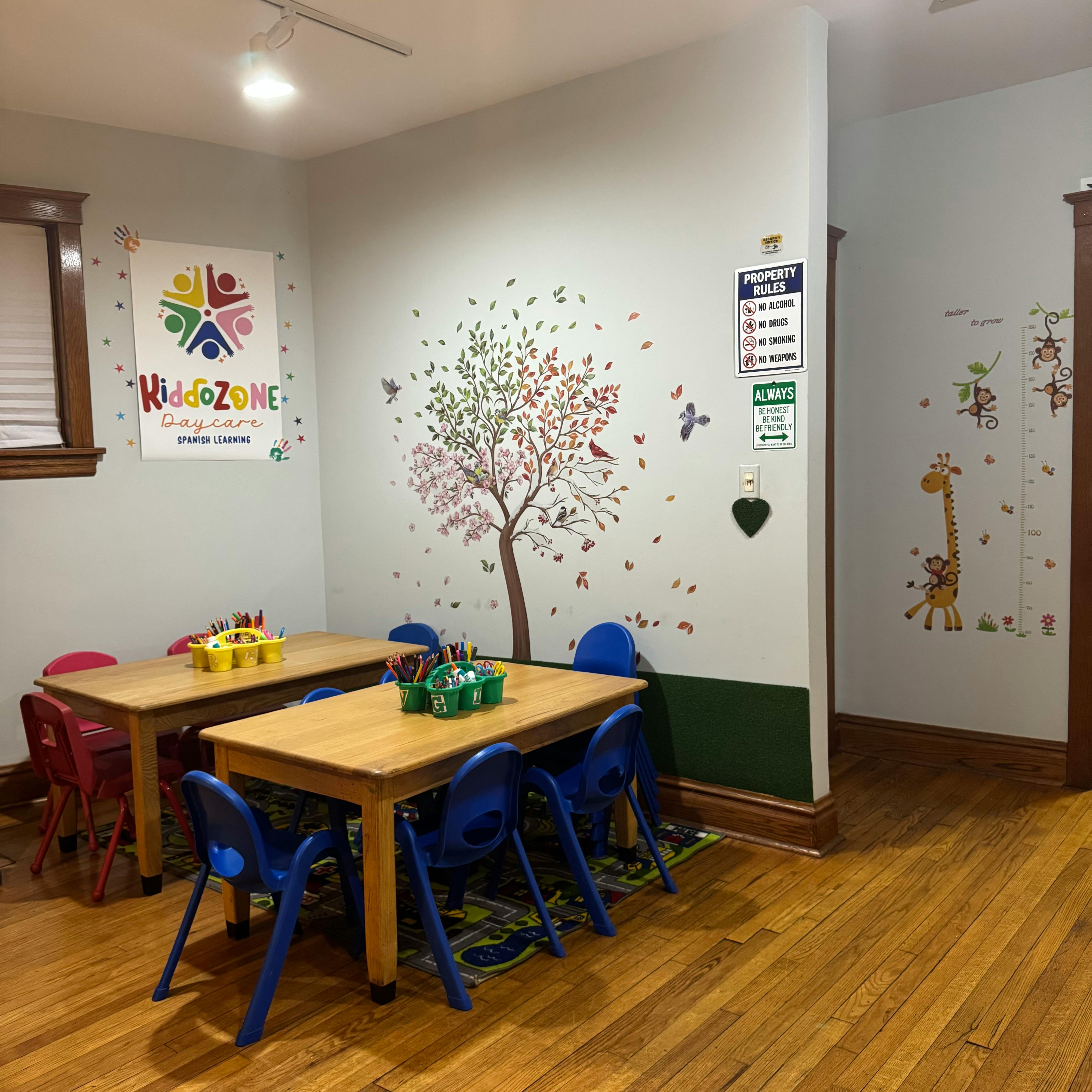 Classroom with small tables and chairs, wall decals of trees and giraffes