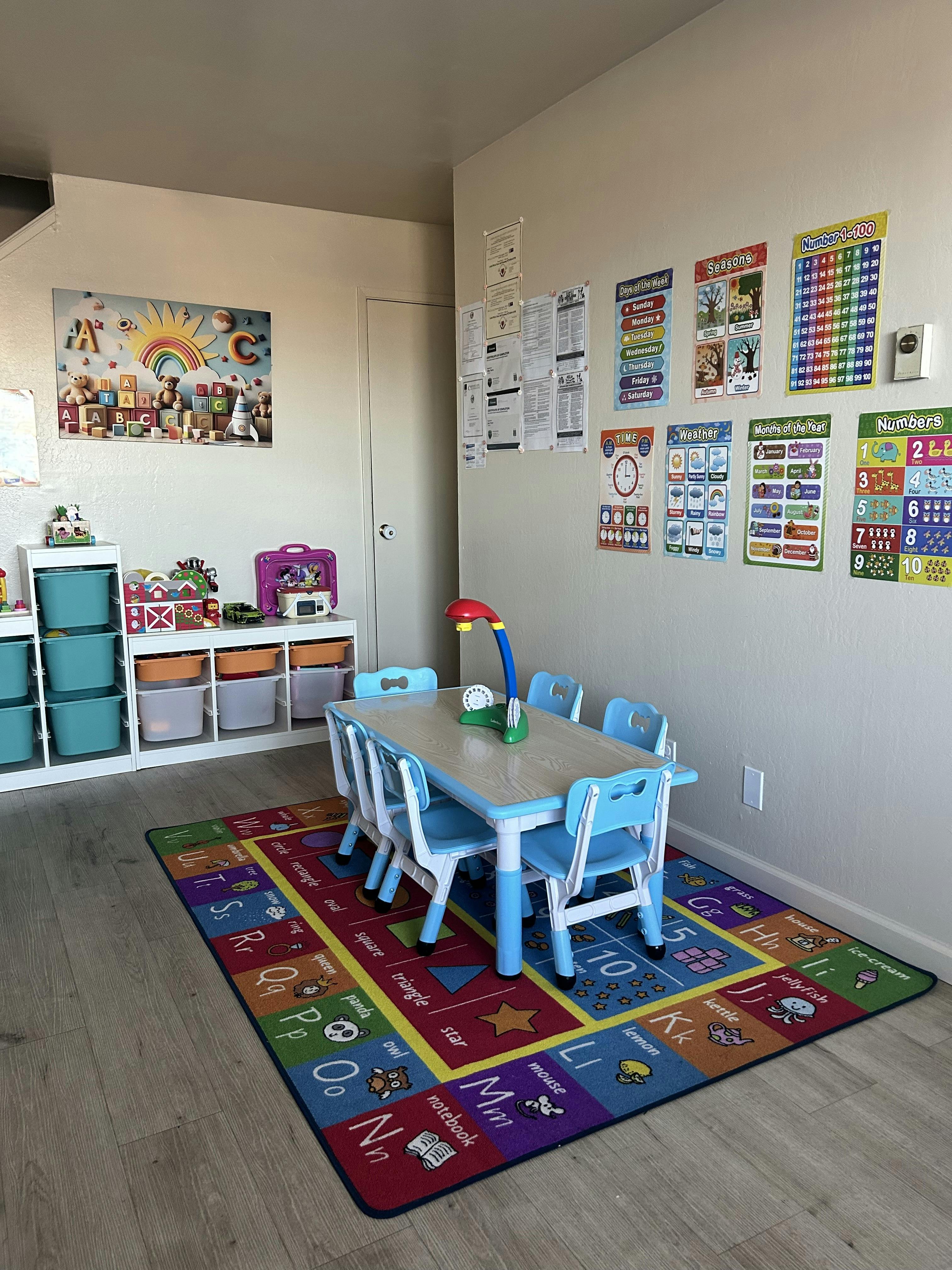 A classroom with a small table and chairs, storage bins, and educational posters