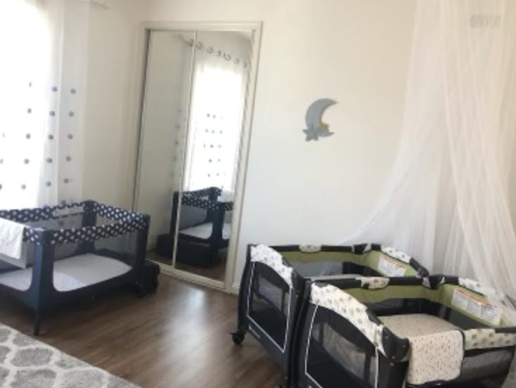 Three baby cribs in a room with a mirror and sheer curtains