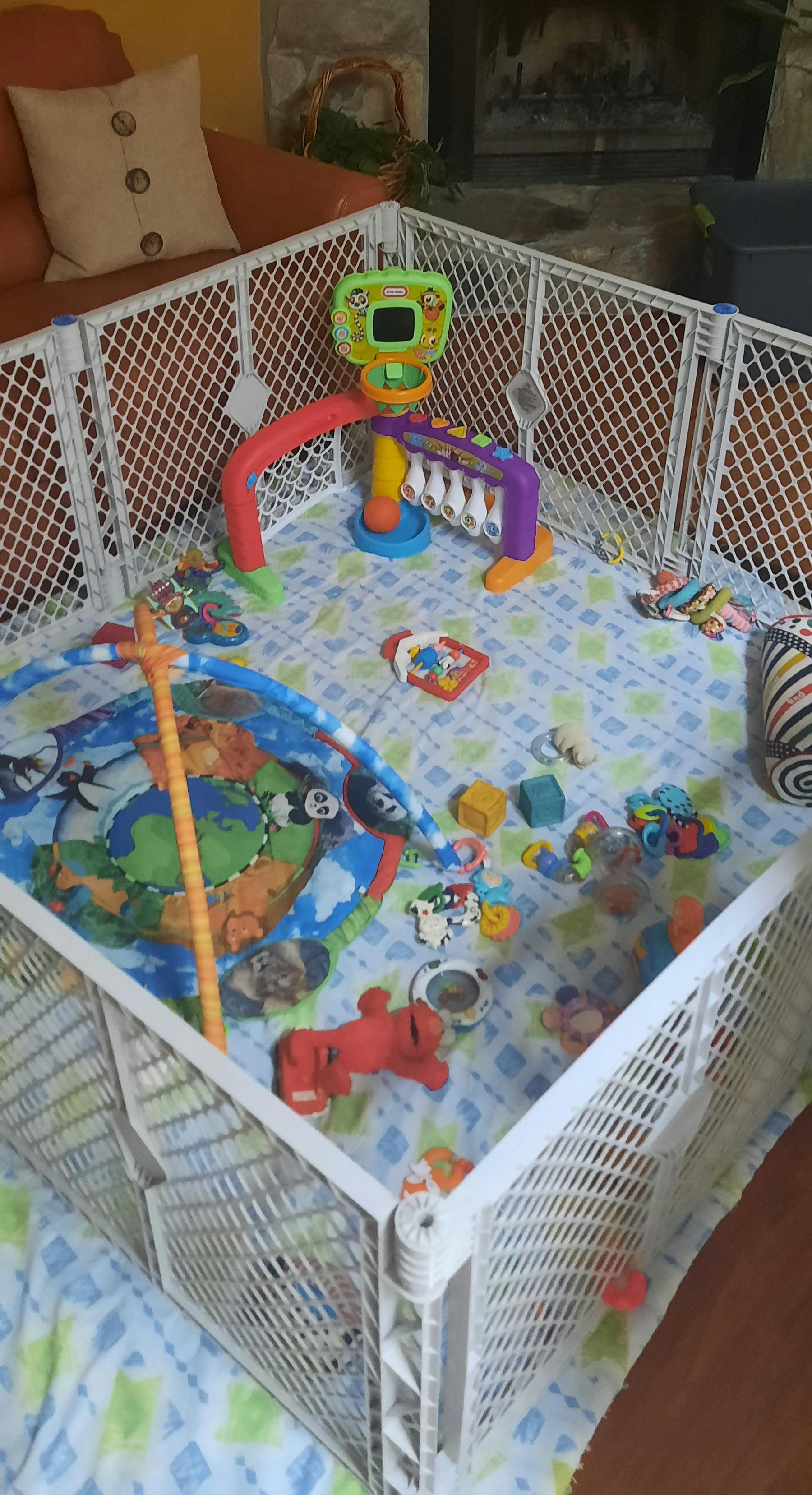 Baby playpen filled with assorted developmental toys and a play mat