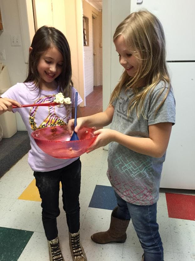 Two children mixing ingredients in a red bowl