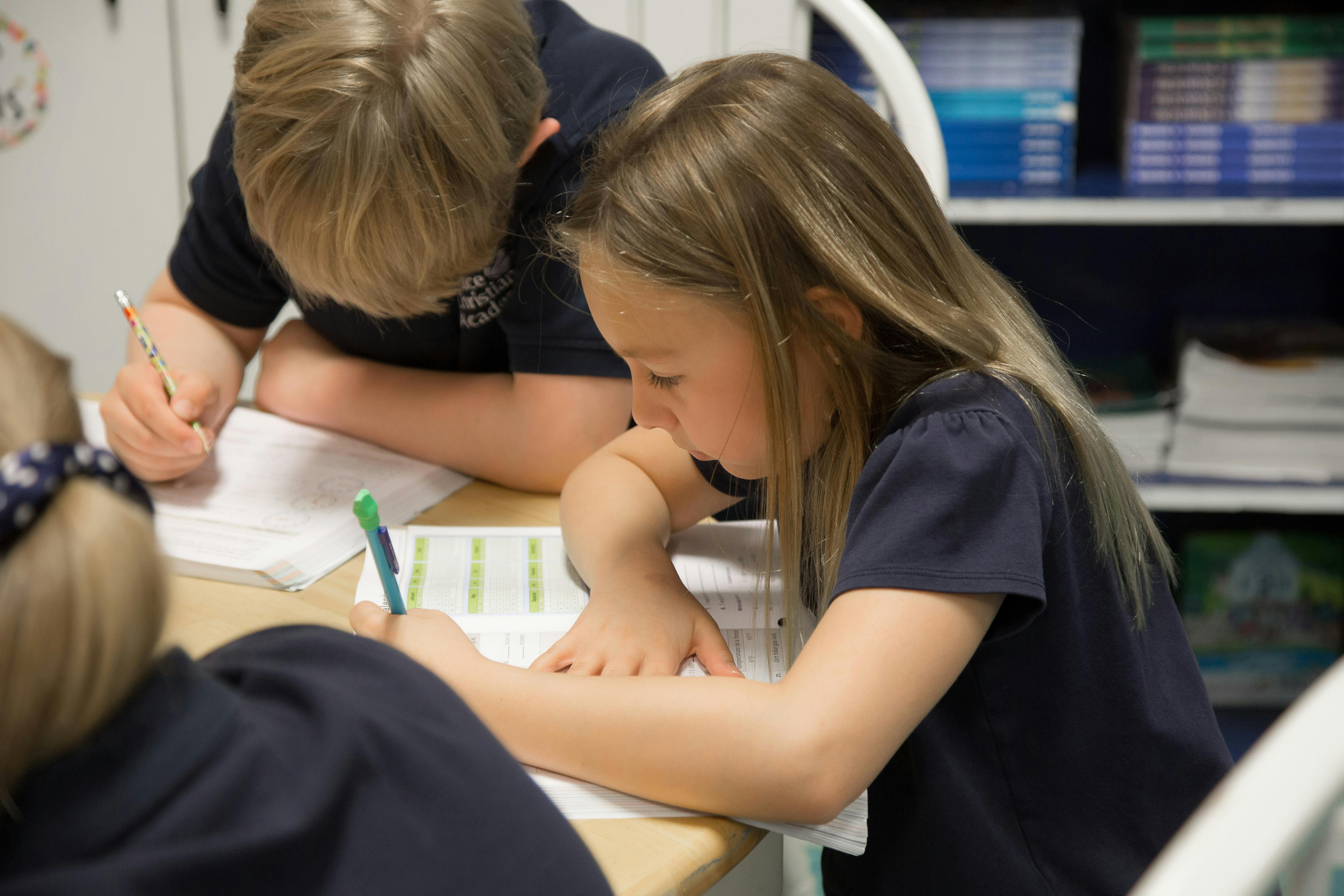Three children writing at a desk in a classroom