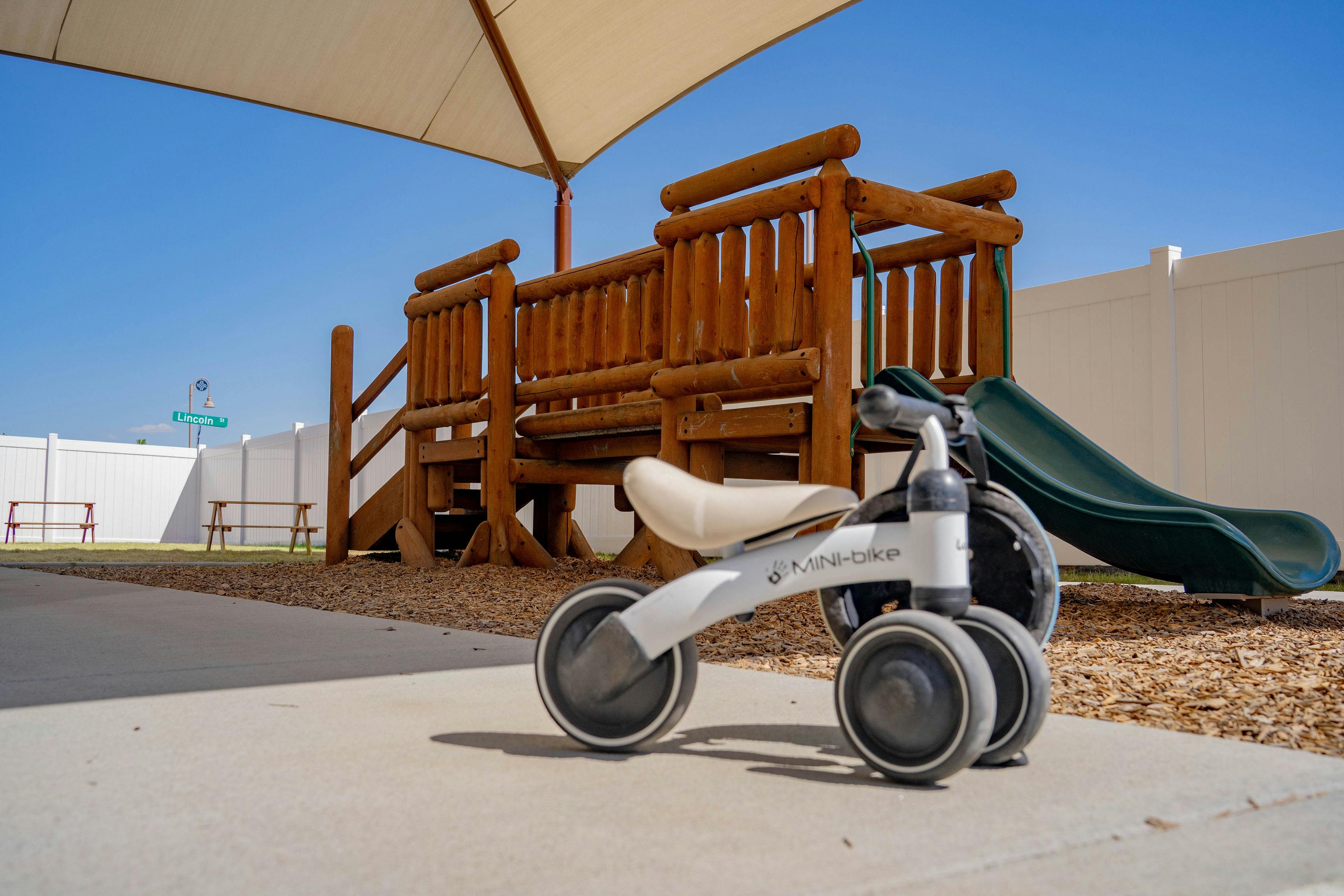 White tricycle in front of a wooden playground with a green slide
