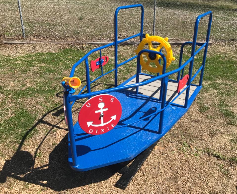 Blue boat-shaped playground equipment with a yellow steering wheel and red anchor sign