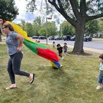Person running with a colorful parachute, children in background