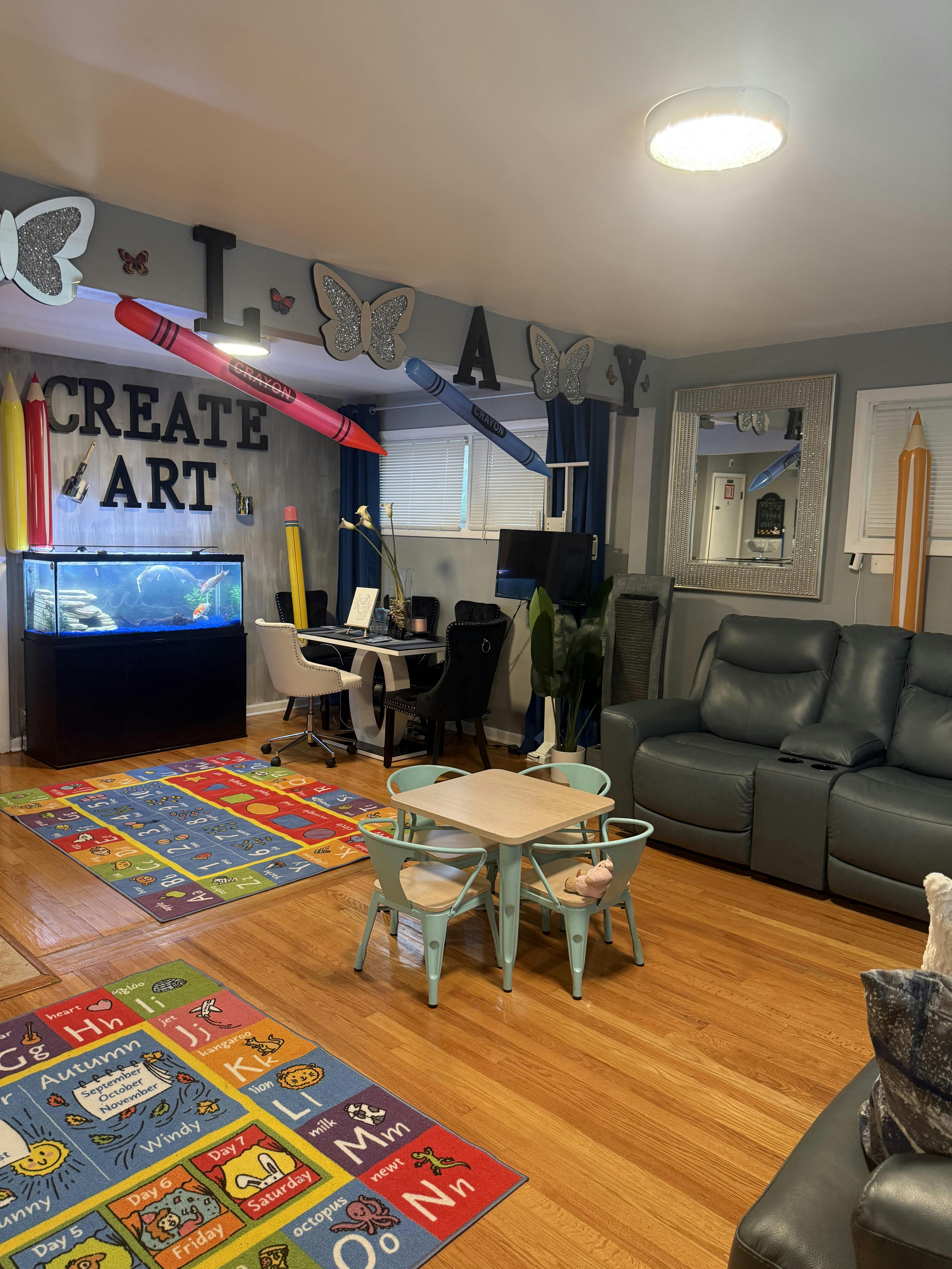 Room with "CREATE ART" on wall, fish tank, desk, small table with chairs, and rugs