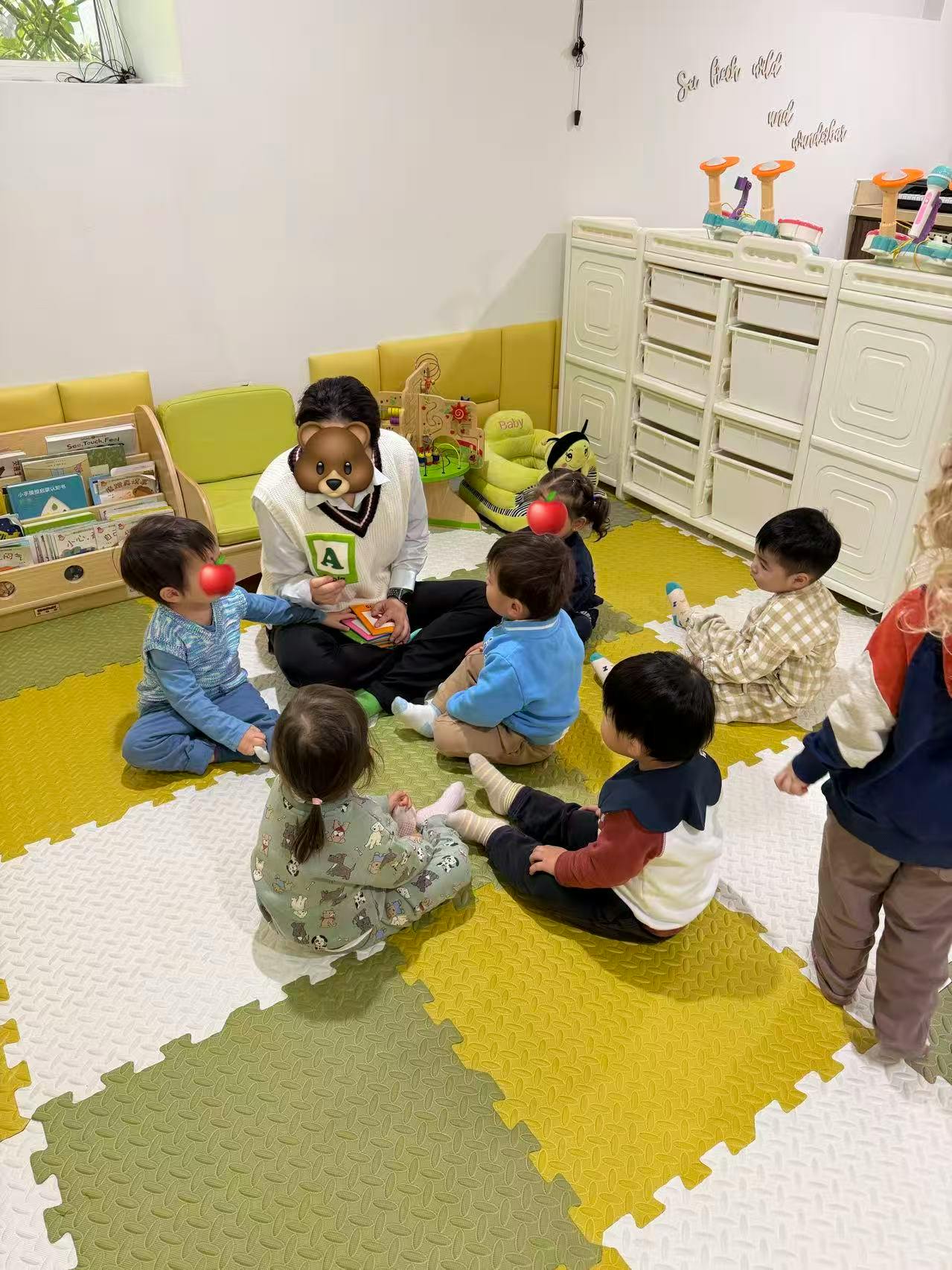 Adult sitting on floor with several children around holding up a card with 'A'