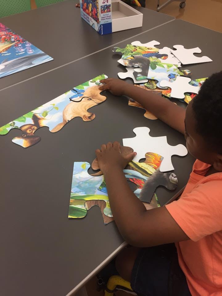Child's hands assembling a large floor puzzle on a table
