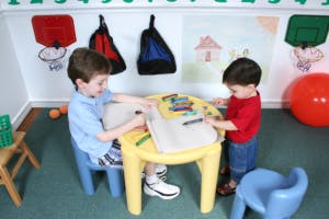 Two children drawing at a small yellow table in a room