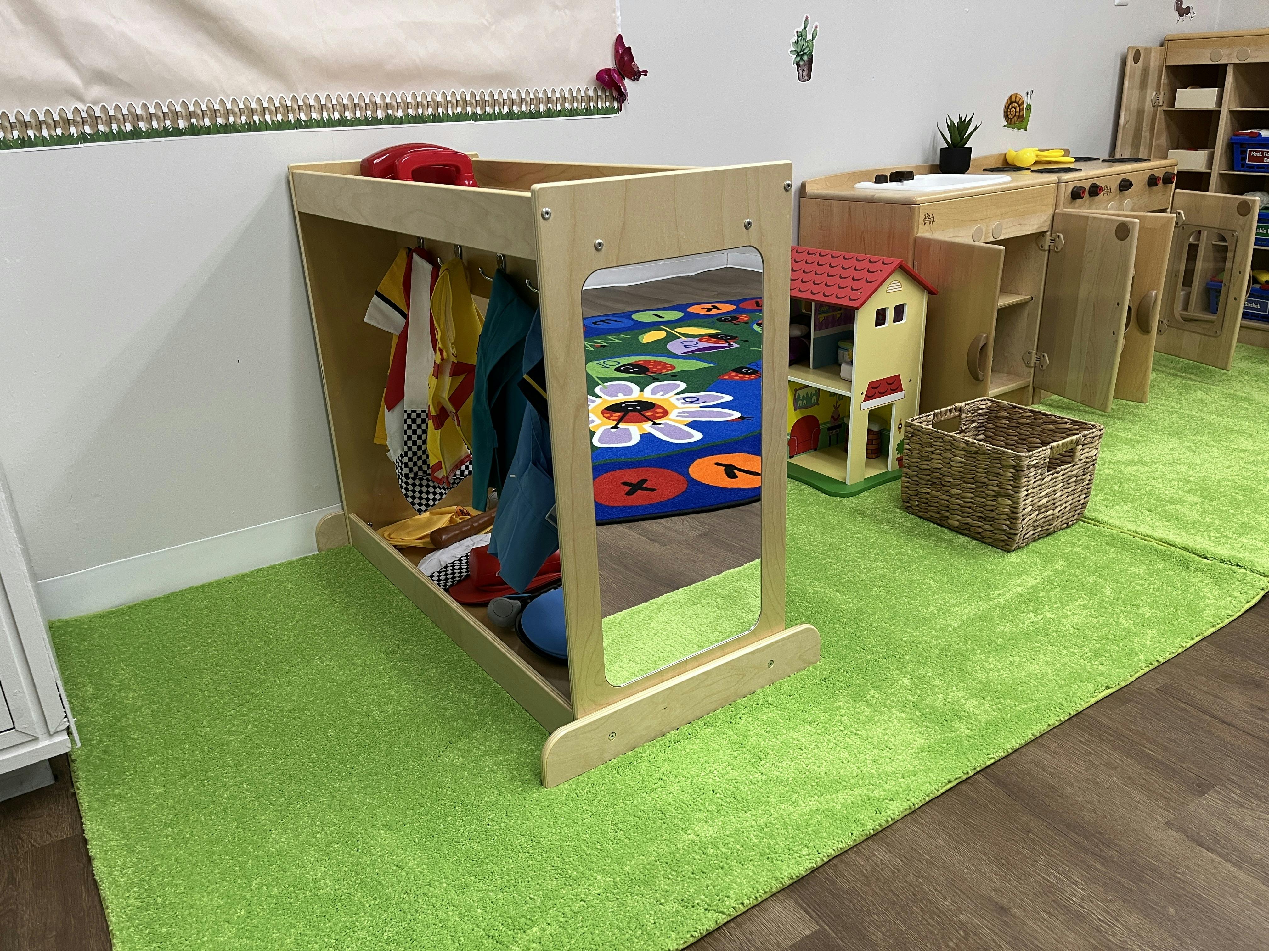 Wooden dress-up rack and play kitchen in a playroom with a green area rug