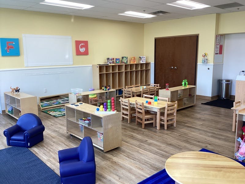 Classroom with small tables and chairs, shelves with toys, and a whiteboard