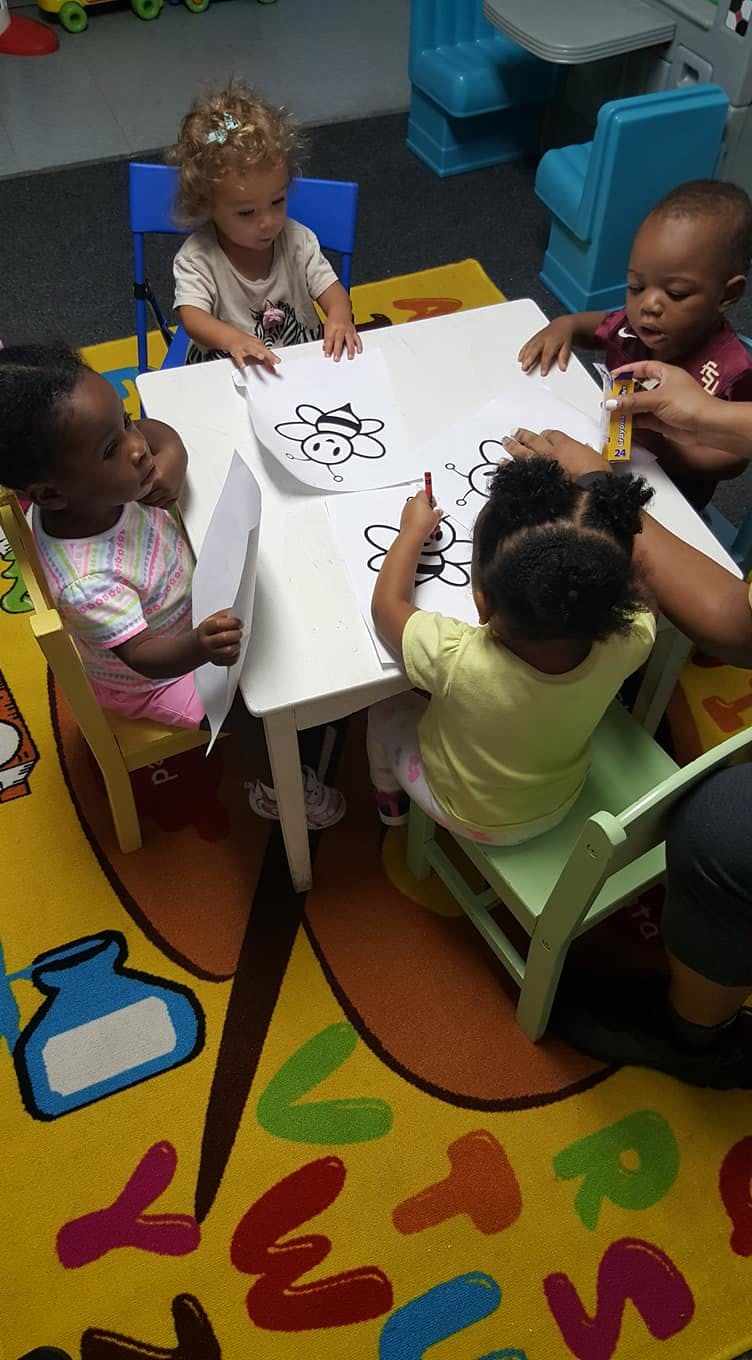 Four children coloring at a small white table