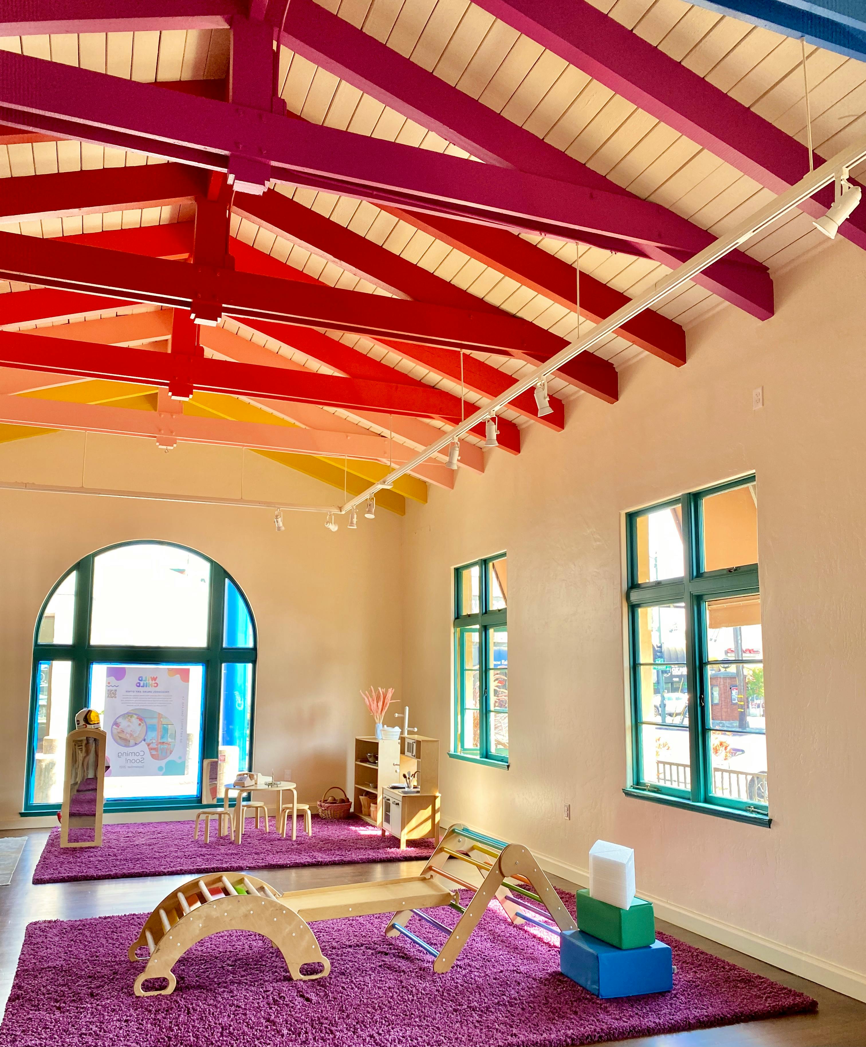 Playroom with colorful ceiling beams, windows, and play equipment on purple rugs