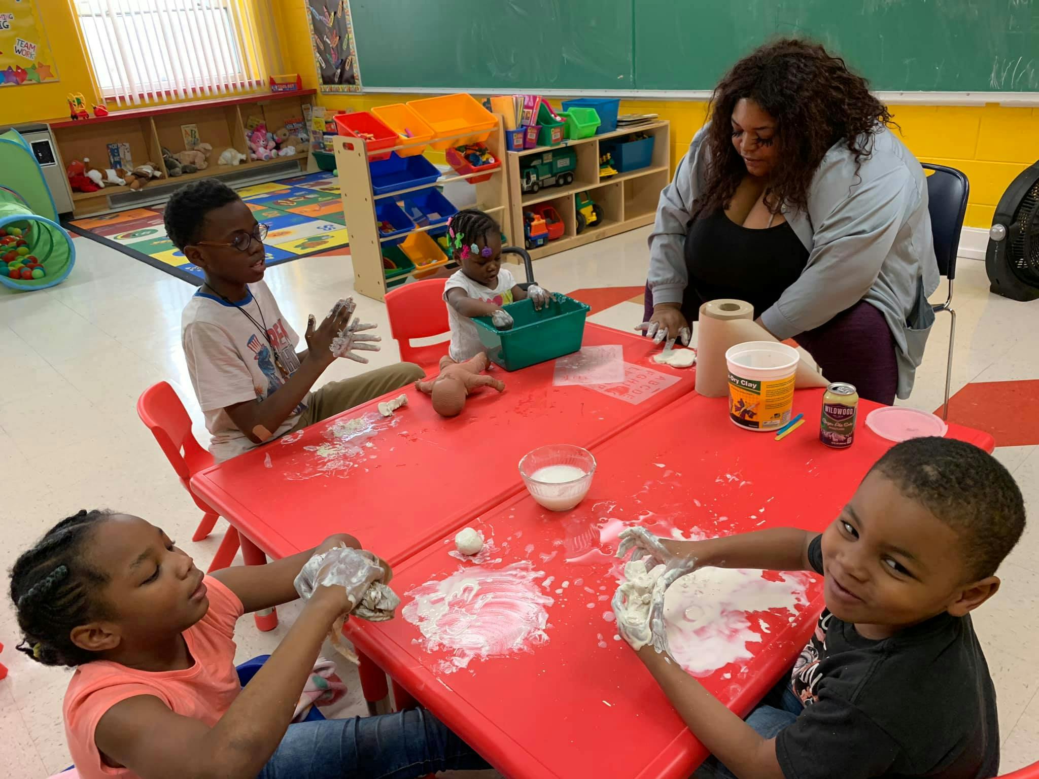 Adult and children at a red table playing with white dough