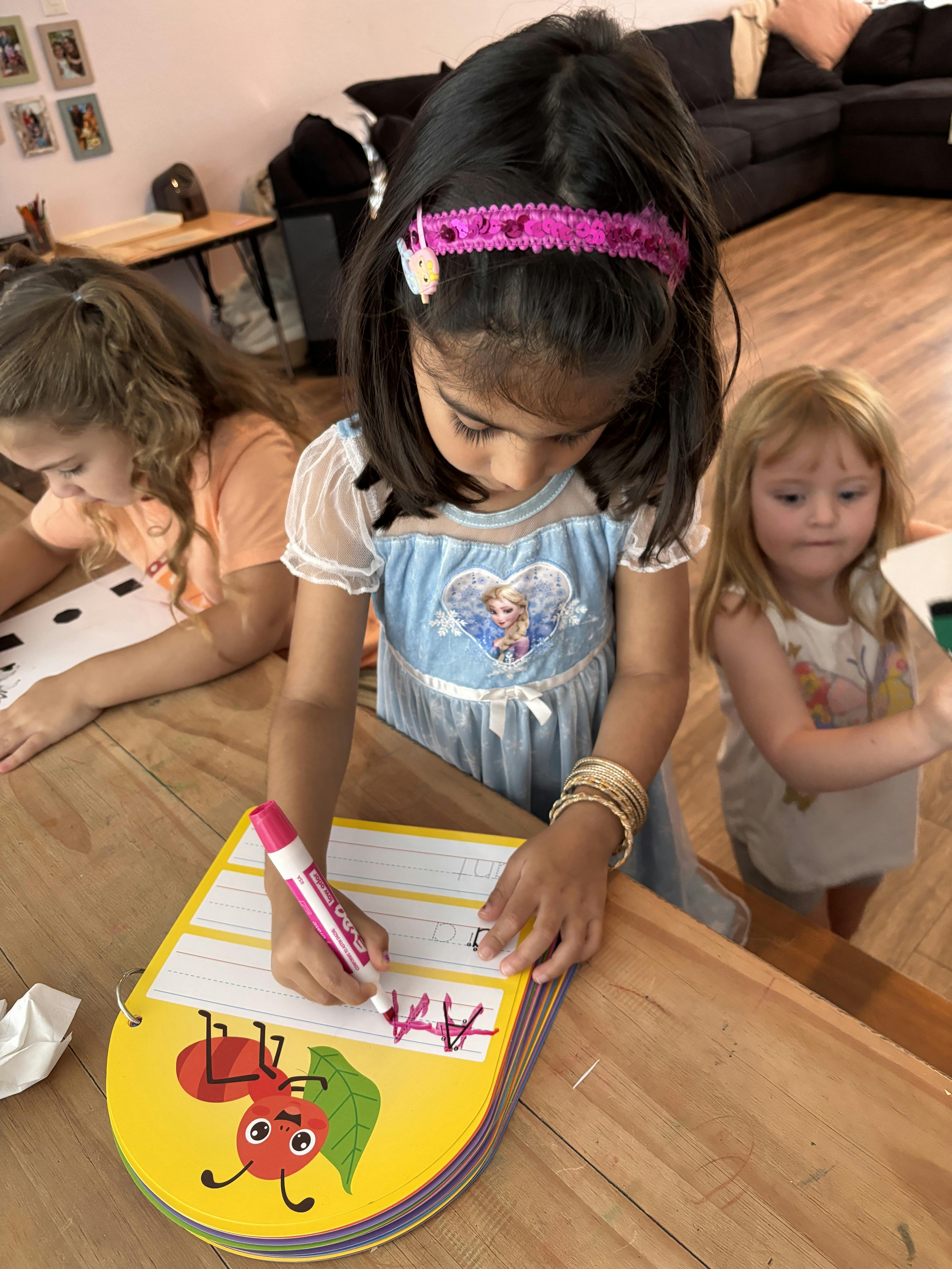 Child writing on a yellow book with a marker, other children nearby