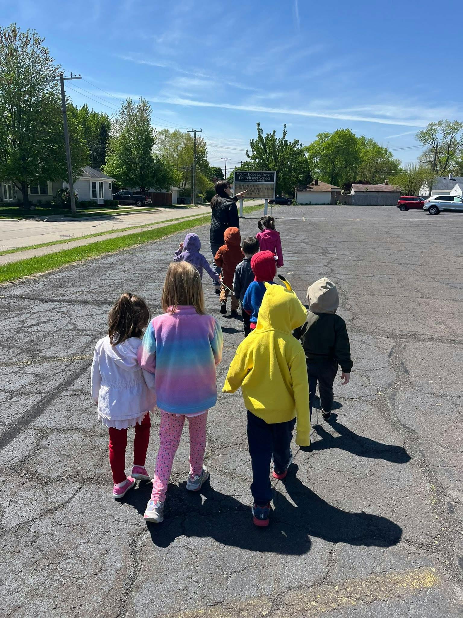 Adult leading a line of children on a paved surface outdoors area