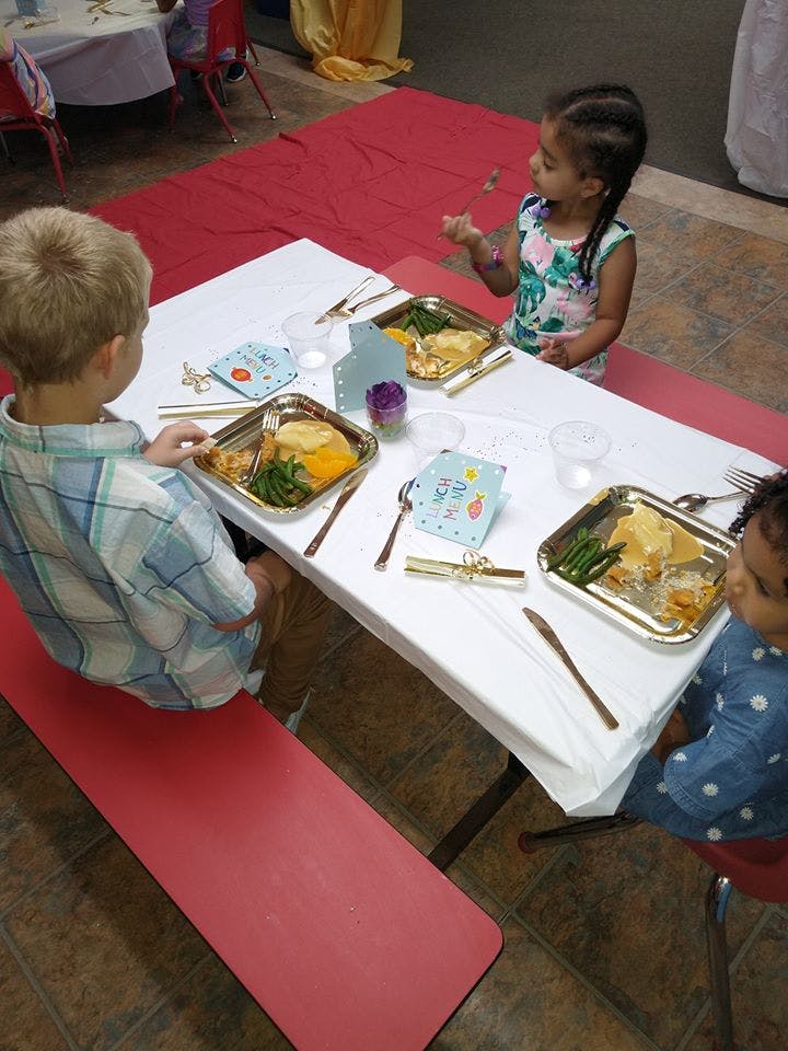 Three children sitting at a table with plates of food