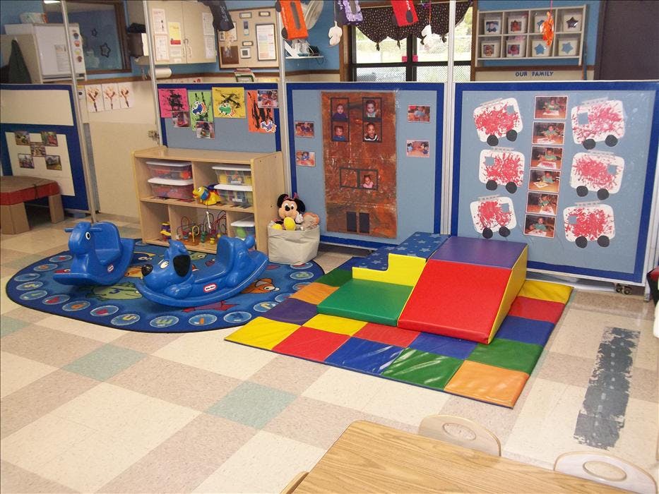 Classroom with rocking toys, colorful play mat, and shelves