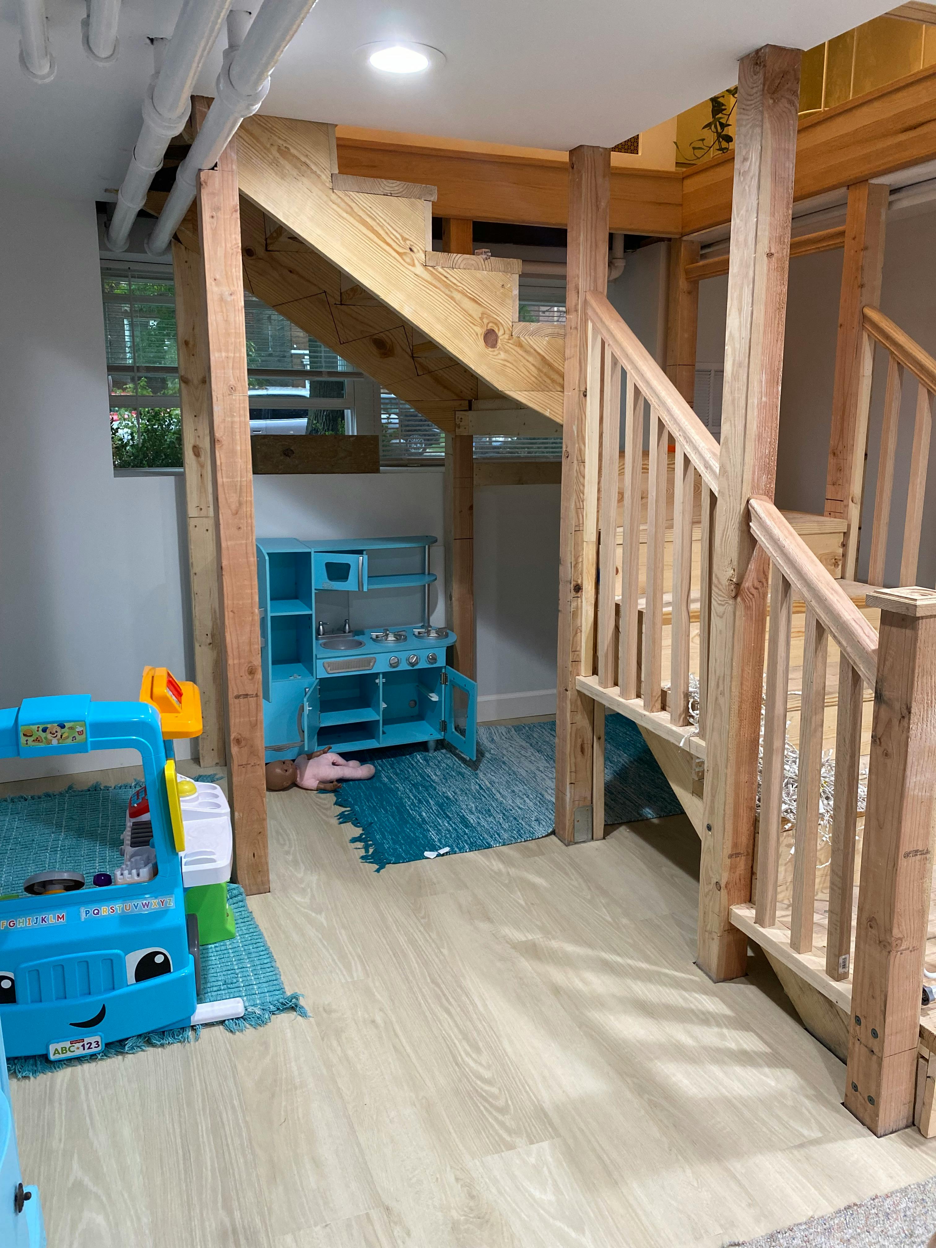 Wooden play structure with stairs and a blue toy kitchen underneath