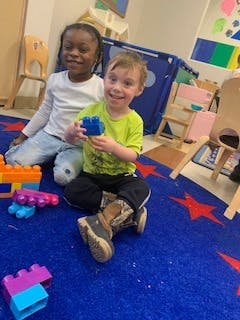 Two children playing with building blocks on a blue rug