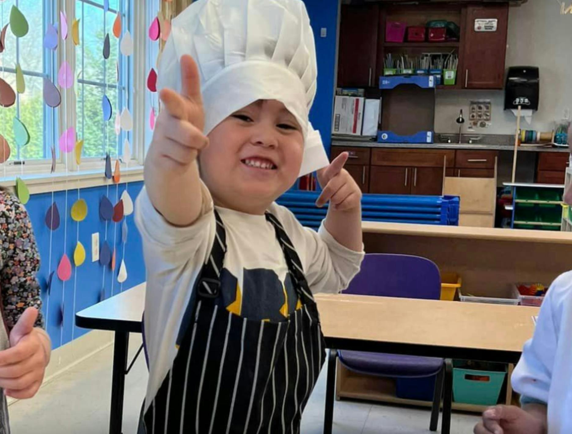 Child in chef hat and apron pointing forward