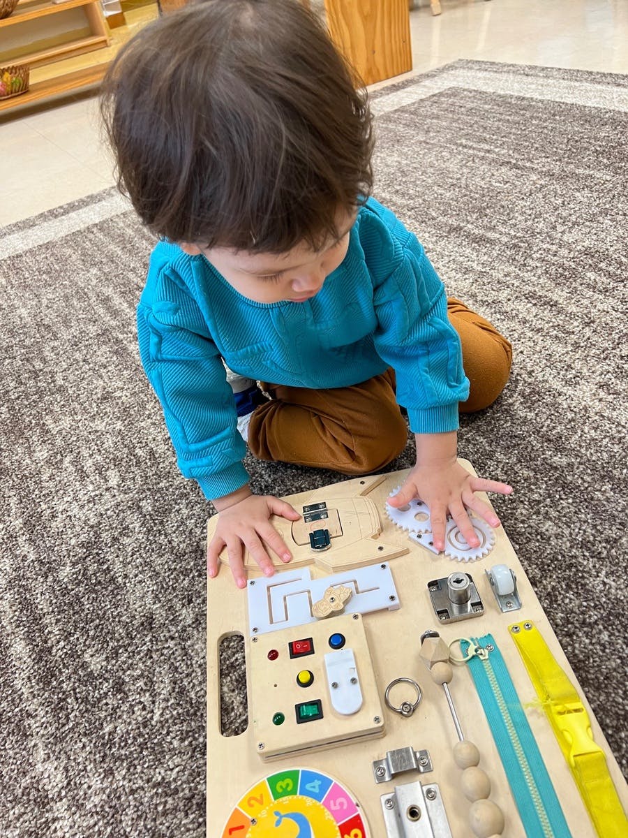 Child playing with a wooden busy board on the floor