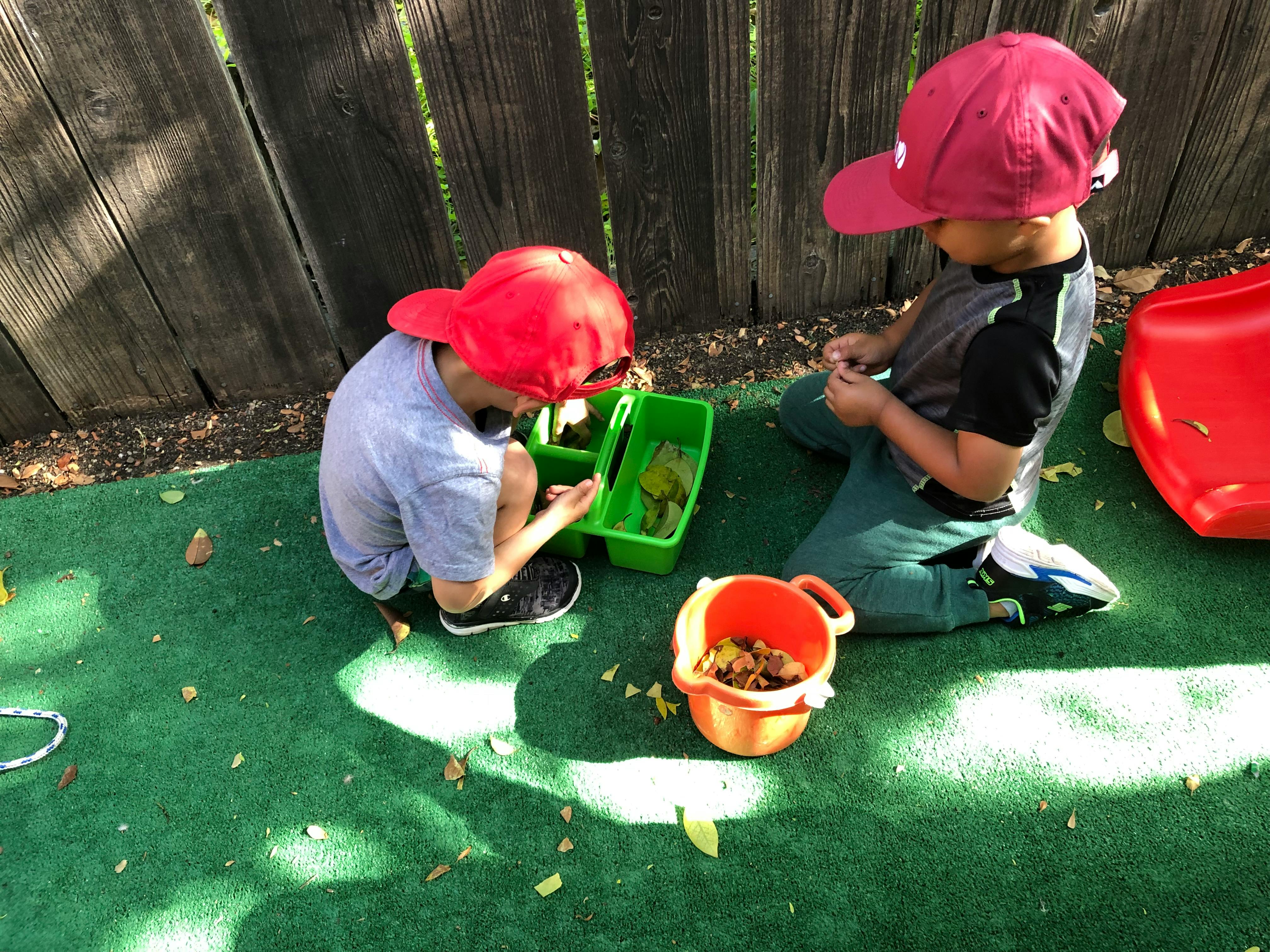 Two children playing with leaves in containers on a playground
