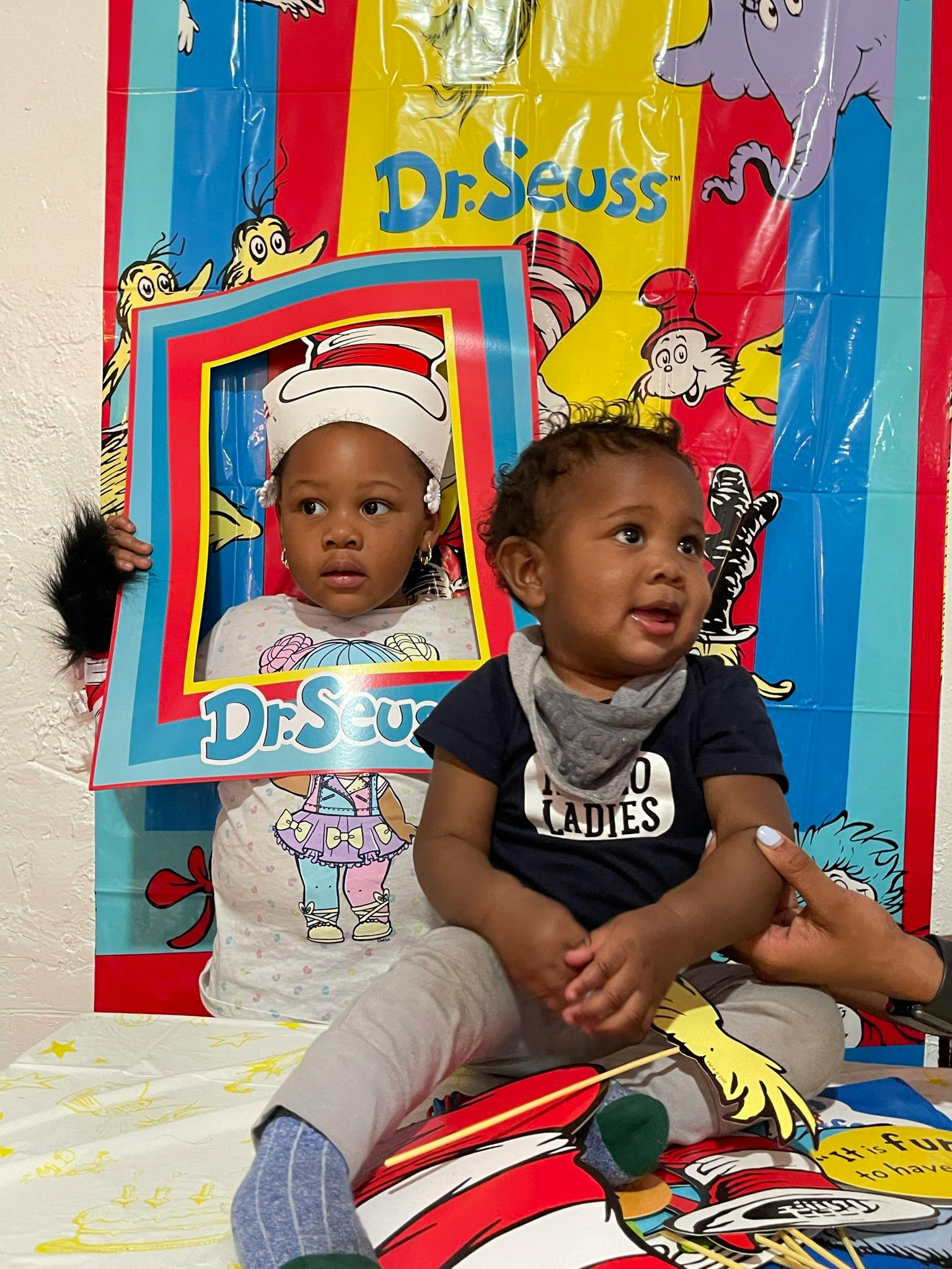 Two children in front of a Dr. Seuss backdrop, one in a Cat in the Hat frame