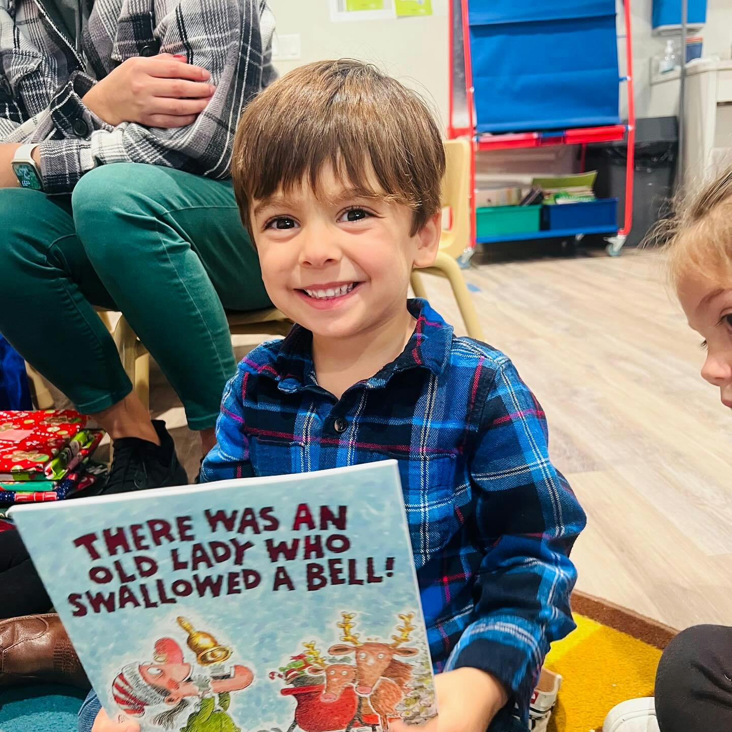 Child holding a book titled "There Was an Old Lady Who Swallowed a Bell!"