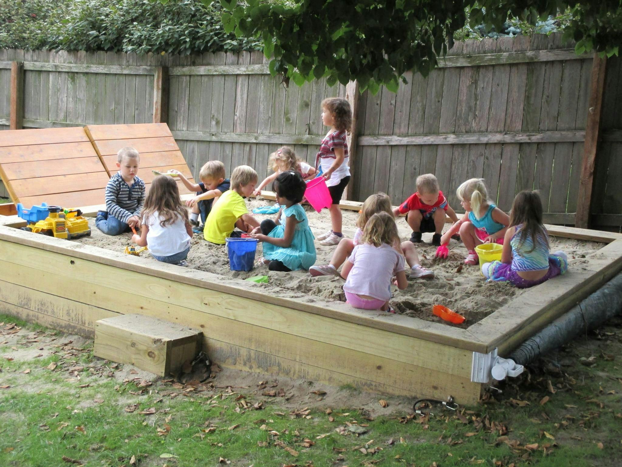 Children playing in a large sandbox with toys