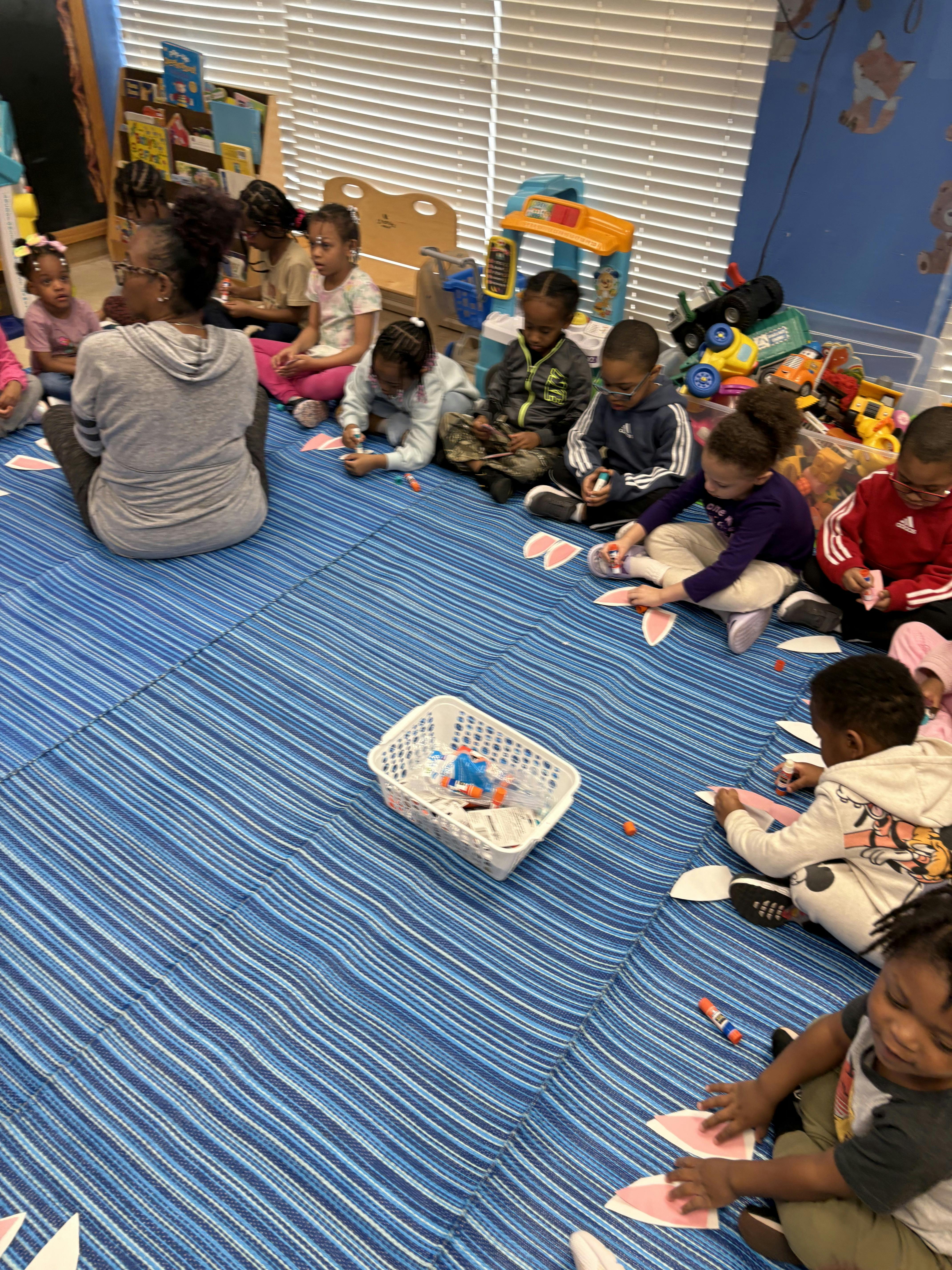 Adult and children sitting on a blue mat doing crafts