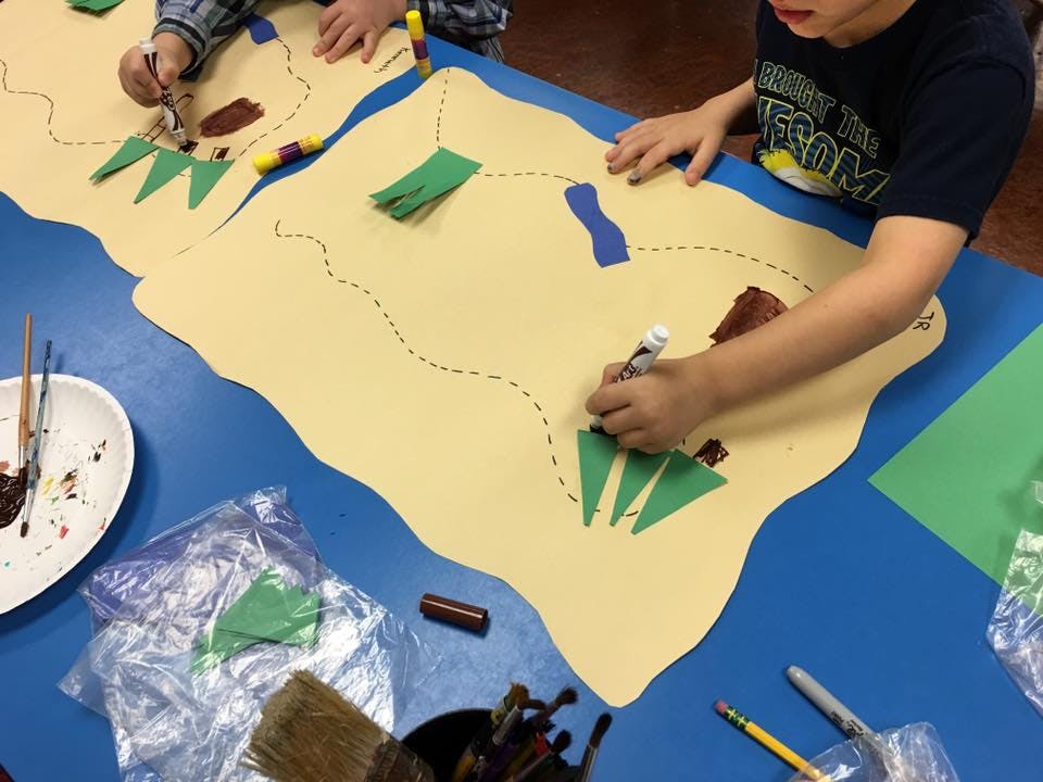 Child drawing on a large paper map with cutouts